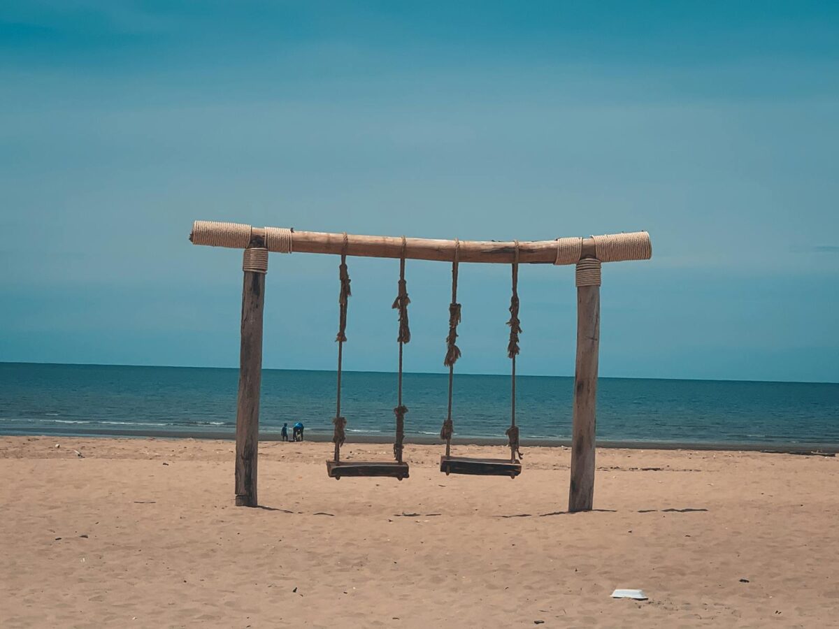 Rustic wooden swing set on a serene beach in Cha-am, Thailand, under a clear blue sky.