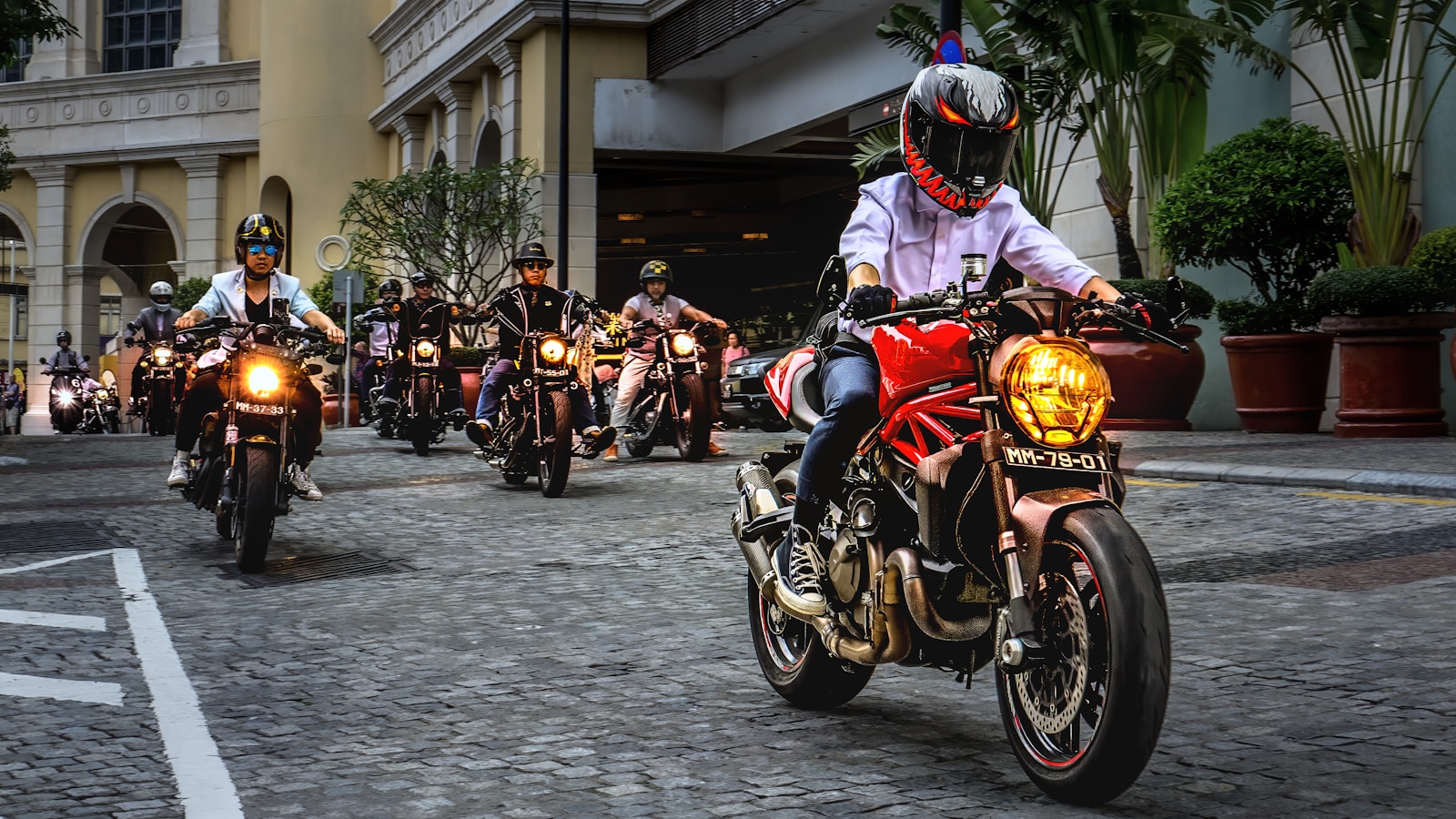 Motorcyclists ride together down a brick road.